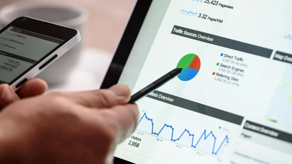 Hand using a stylus to point at a traffic sources pie chart on a tablet displaying web analytics.