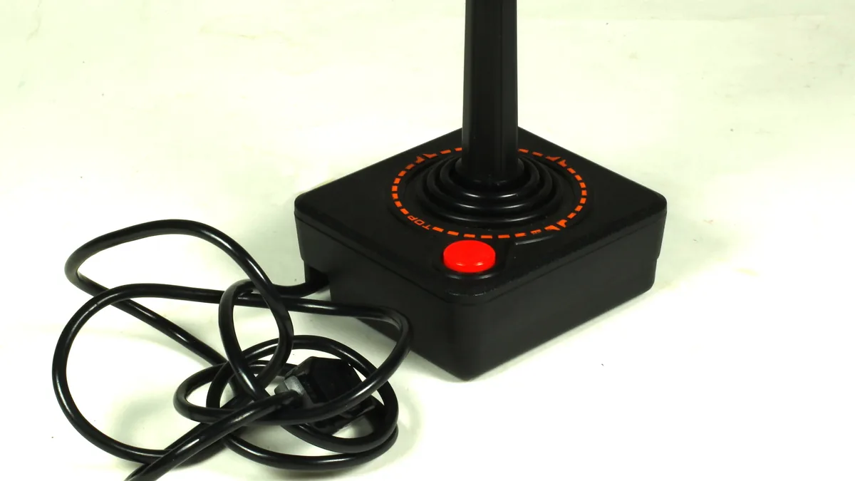 Classic black Atari joystick with red button and orange markings, coiled cable on a white surface.