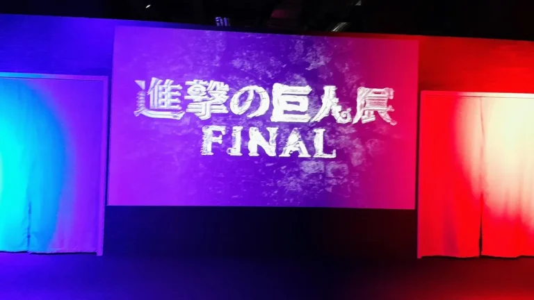 Colorful stage screen showing the stylized Attack on Titan Exhibition FINAL logo in Japanese and English.