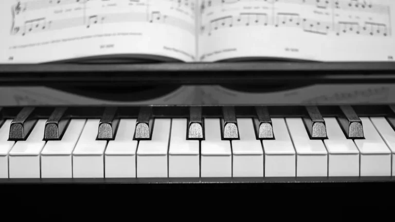 Black and white close-up of piano keys with sheet music in the background.