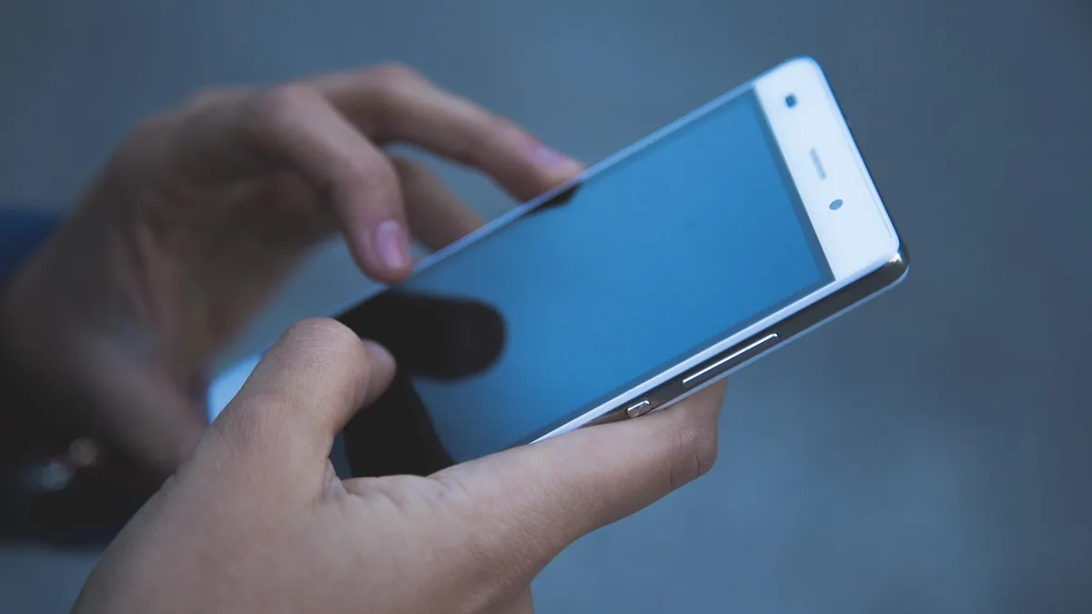 Close-up of hands holding and typing on a white smartphone with a blue screen.