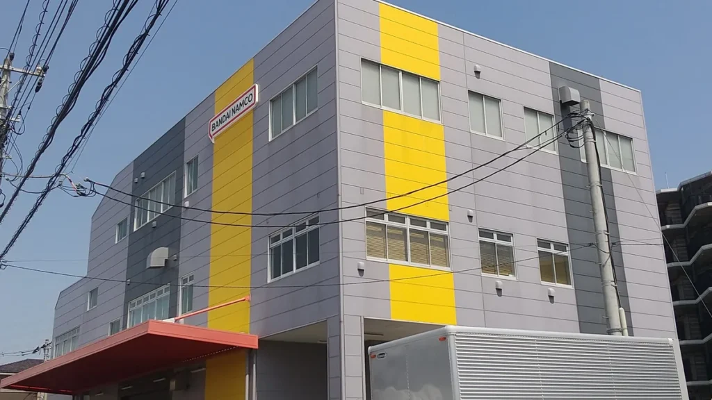 A grey building with bold yellow vertical stripes and the red Bandai Namco logo on the side.