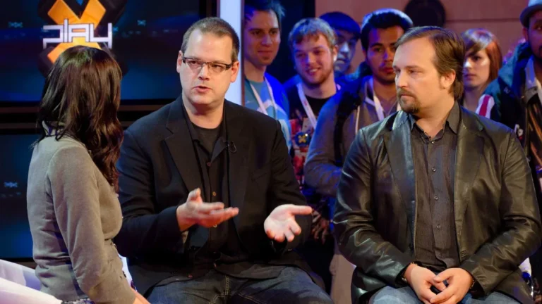 Greg Zeschuk speaks in a gaming interview alongside Ray Muzyka, with a PLAY logo in the background.