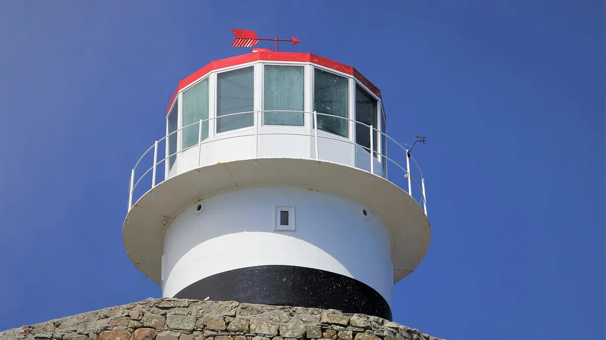A white lighthouse with a red roof and black stripe stands against a clear blue sky.