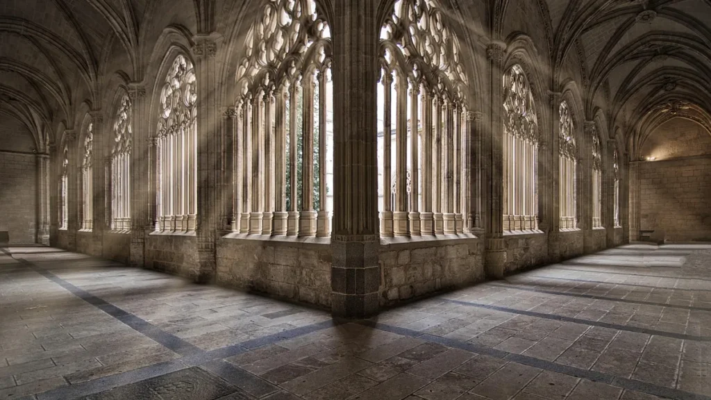Gothic stone cloister with dramatic sunbeams filtering through ornate window arches, evoking a mysterious cathedral