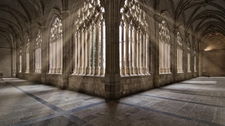 Gothic stone cloister with dramatic sunbeams filtering through ornate window arches, evoking a mysterious cathedral