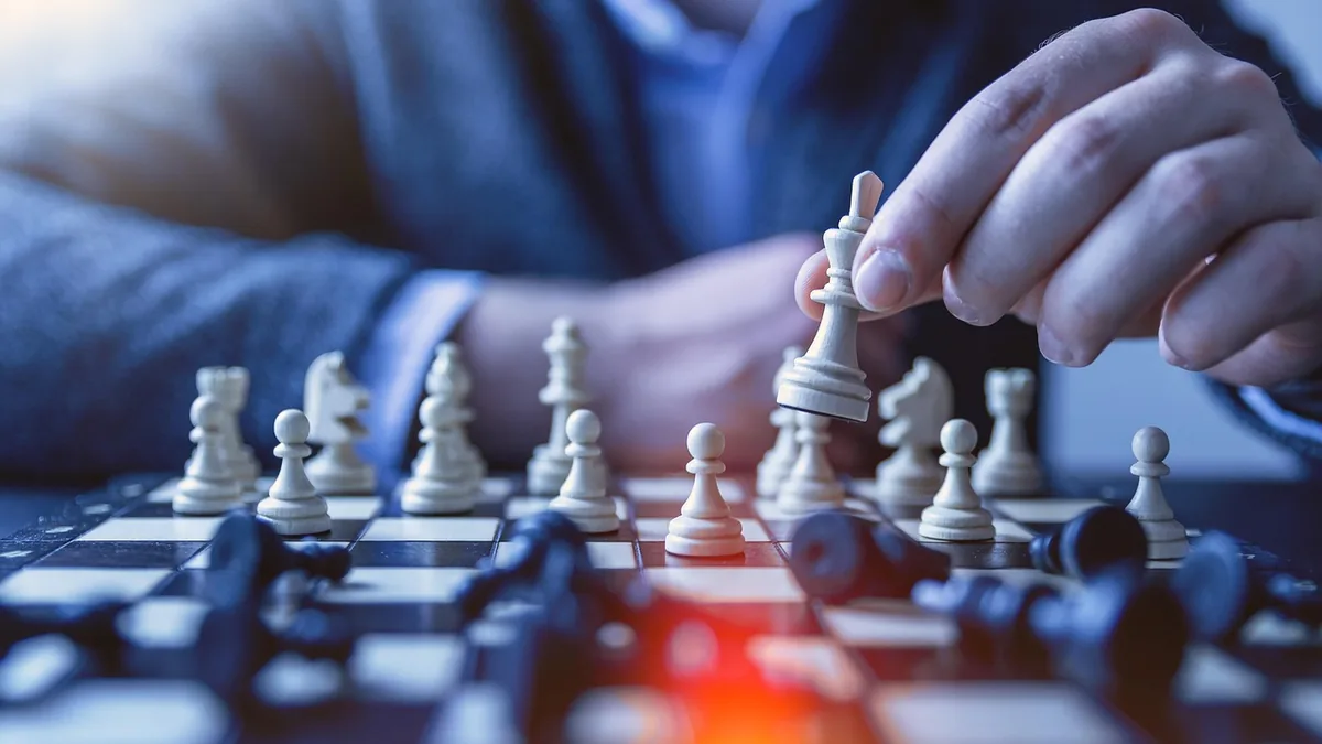 Hand moving a white king piece on a chessboard, symbolizing strategic decision-making and tactical planning.