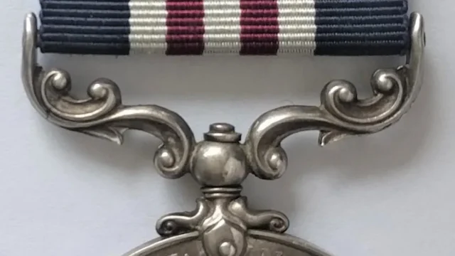 Close-up of a silver military medal with a blue, white, and red striped ribbon.