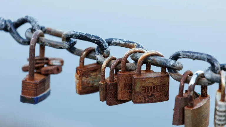 Rusty padlocks, including one engraved with the word EQUIP, locked onto a heavy metal chain.