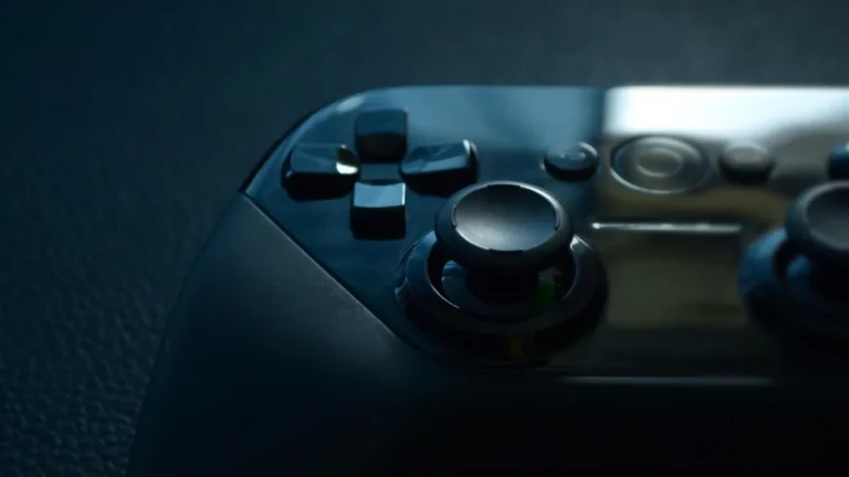 Close-up of a glossy black gaming controller showing the D-pad and analog stick under dark blue lighting.