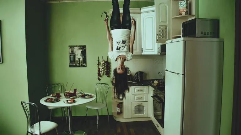 Woman hanging upside down in a surreal green kitchen, creating a creepy horror atmosphere.