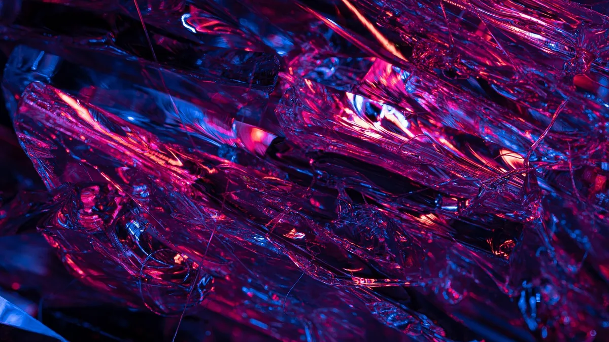 Vibrant neon pink and blue light reflects off sharp, crystalline shards in a futuristic abstract pattern.
