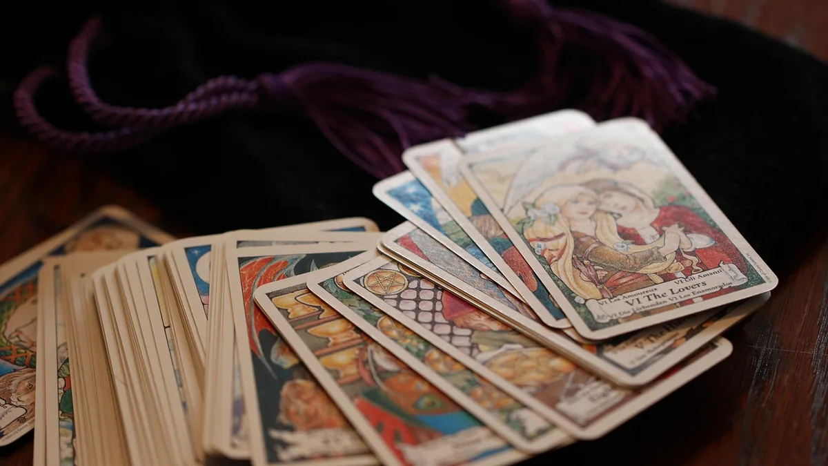 Colorful tarot cards, including VI The Lovers, fanned out on a dark wooden surface near a purple pouch.