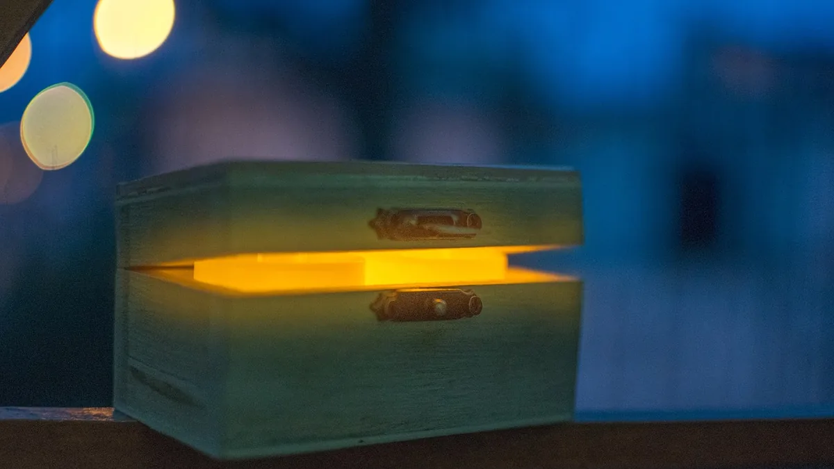 A wooden box slightly open, glowing with warm yellow light against a blurry blue background.
