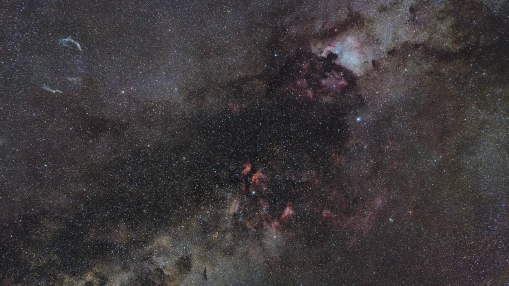 Starry sky showing the Cygnus constellation region, filled with colorful nebulae and bright stars.