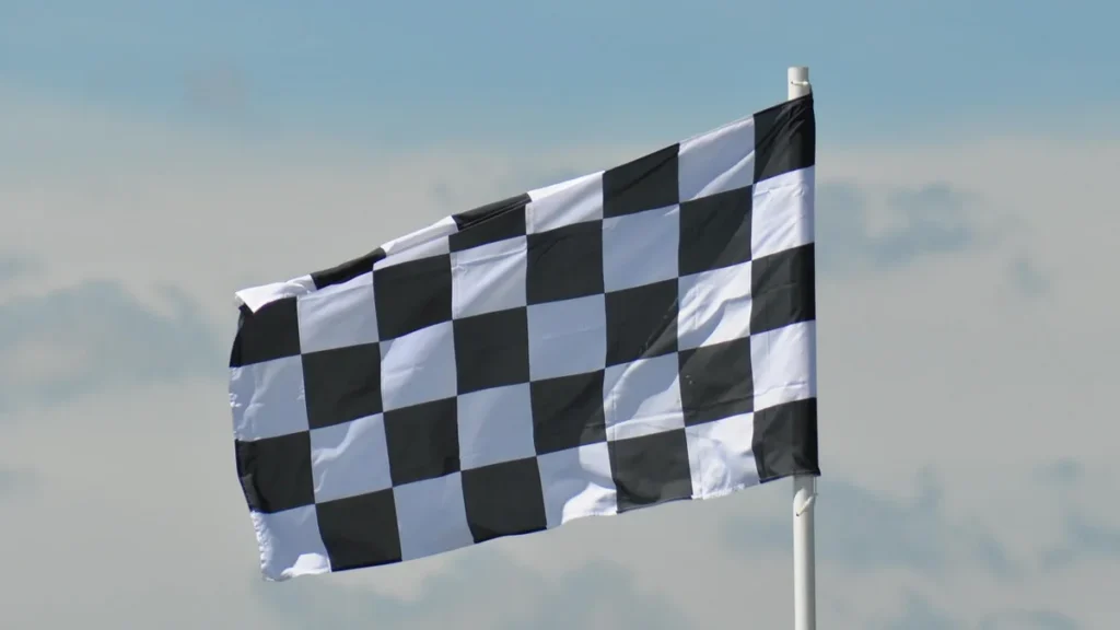 A black and white checkered flag waves on a pole against a cloudy blue sky.