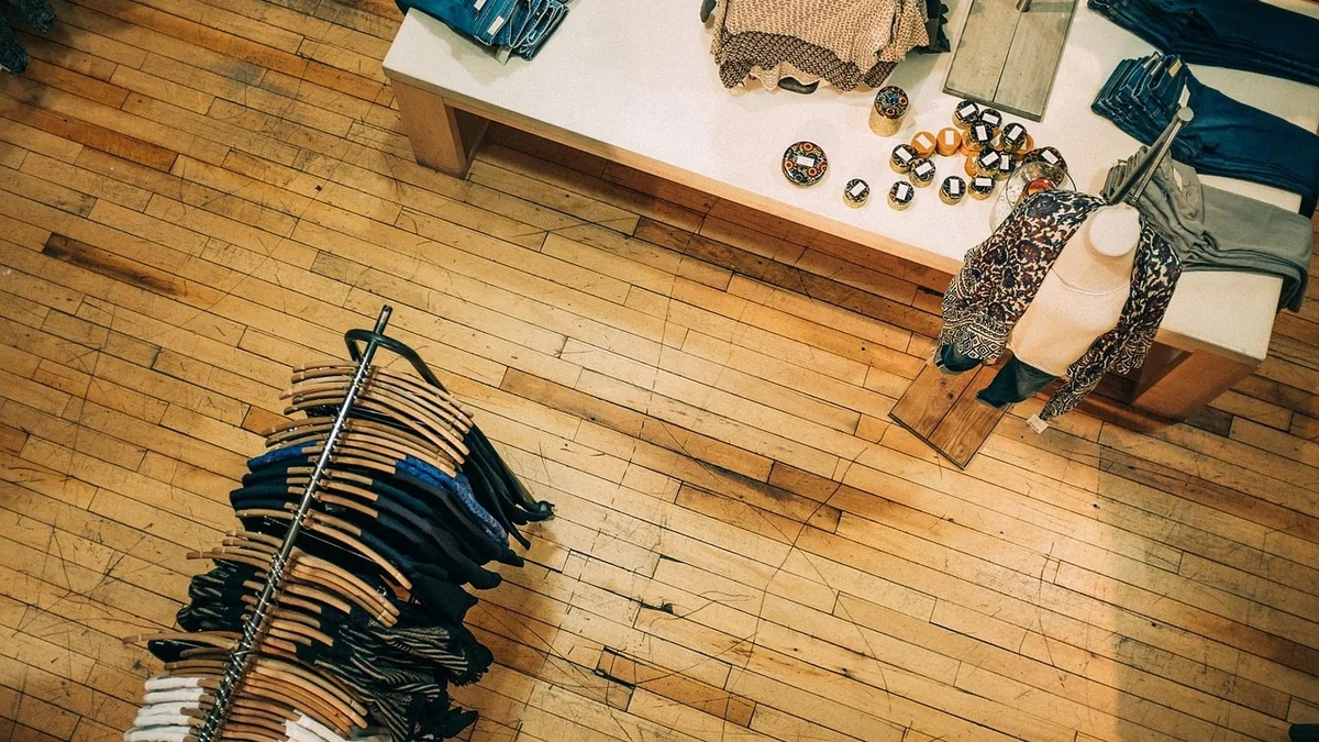 Overhead view of a clothing rack and display table in a boutique store with wooden flooring.