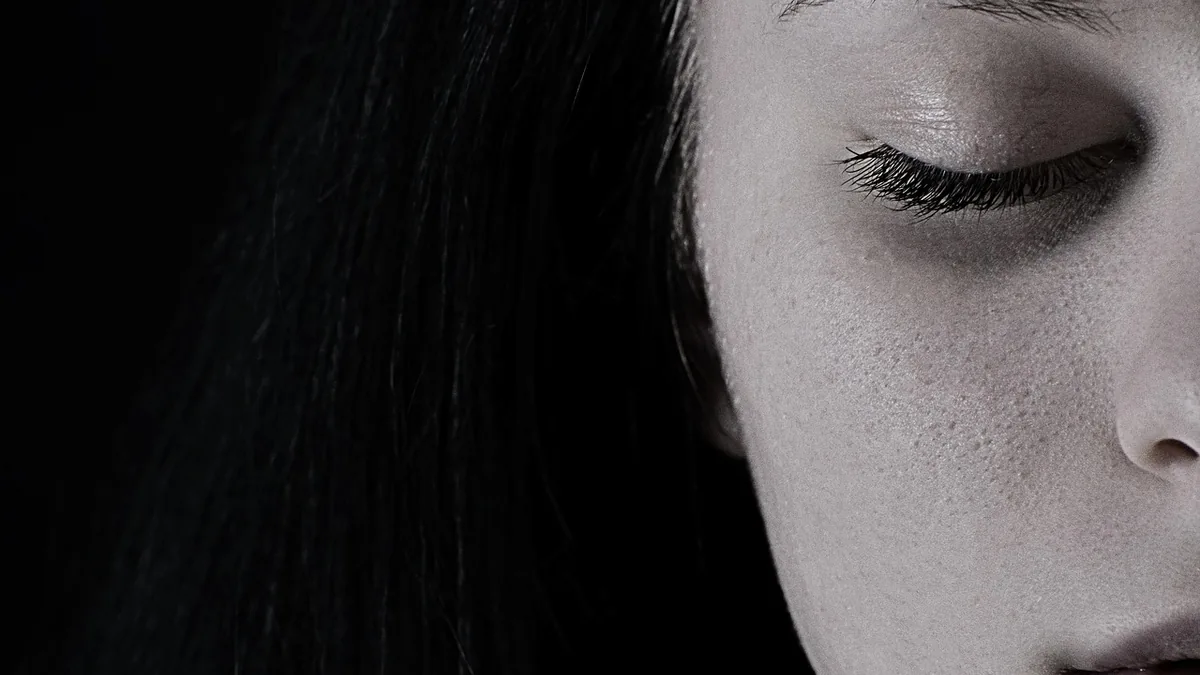 Close-up black and white portrait of a woman with closed eyes, showing detailed skin texture and eyelashes.