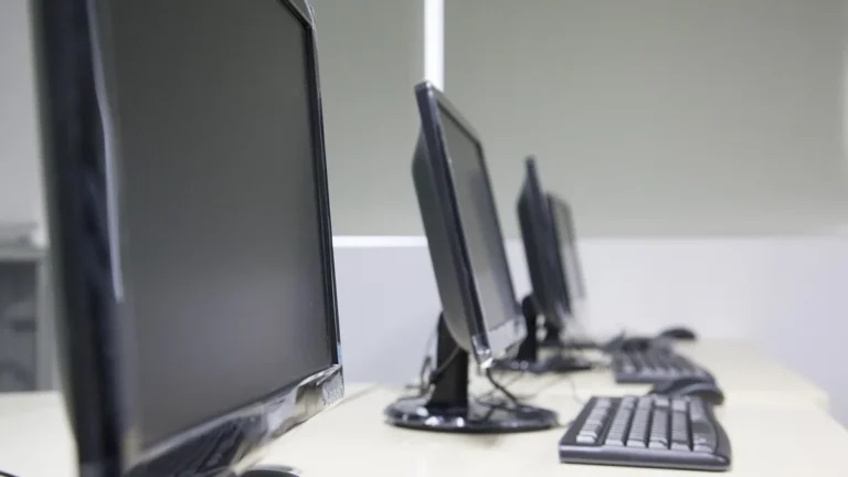 Close-up of black computer monitors and keyboards lined up on an office desk.