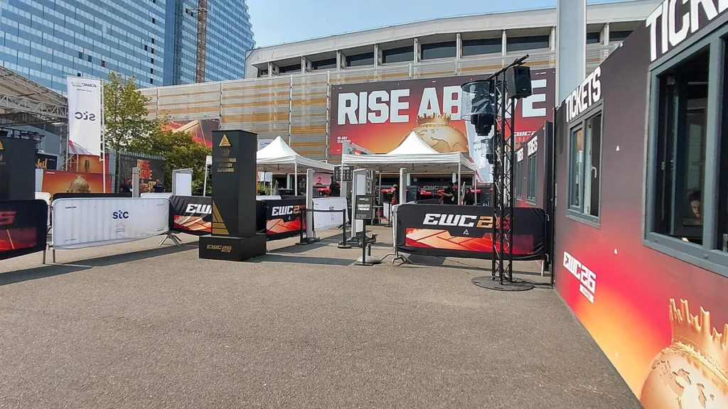 Outdoor view of the EWC 26 venue entrance with ticket booth, barriers, and 'RISE ABOVE' banner.