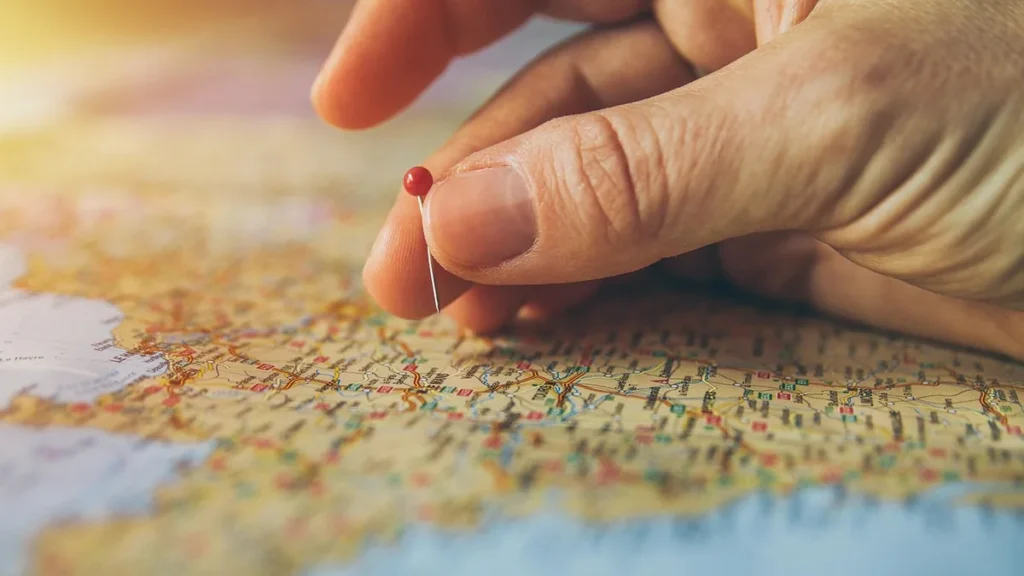 Hand placing a red pin on a colorful geographic map, symbolizing location marking or travel planning.