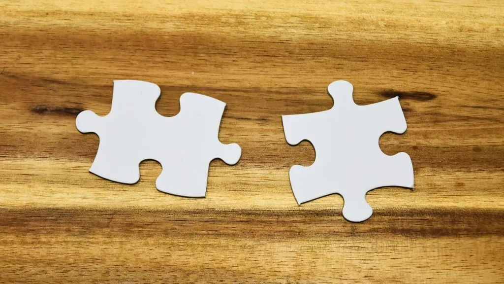 Two blank white puzzle pieces lie side-by-side on a wooden surface, representing integration.