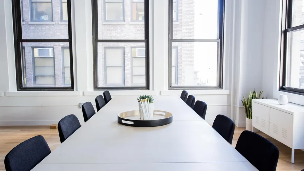 Empty corporate boardroom with a long white table, black chairs, and large windows.