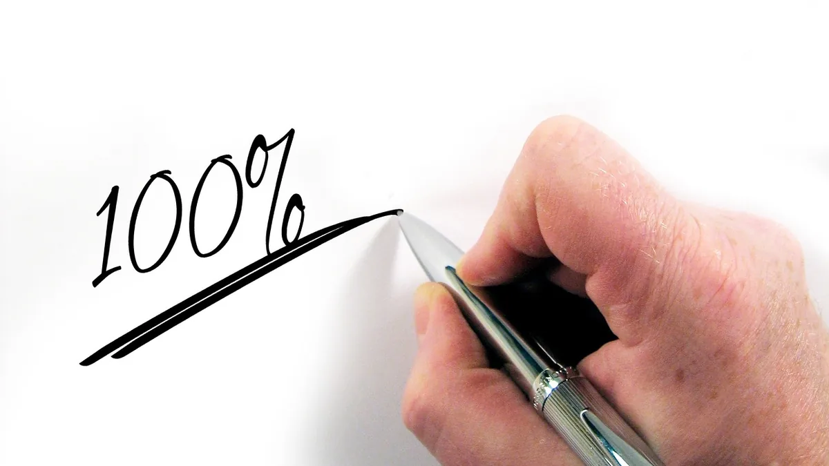 A hand writing '100%' in black ink with a silver pen on a white surface.