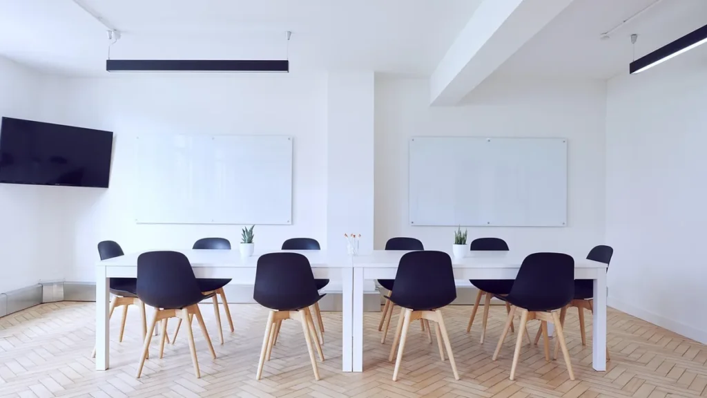 Minimalist white conference room with black chairs and whiteboards on the wall.