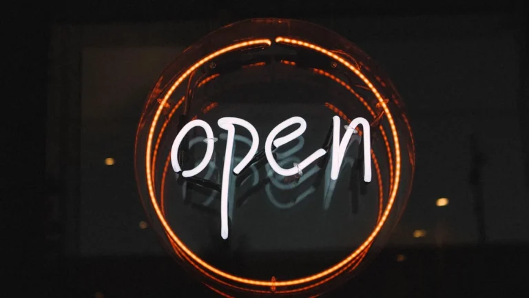 White neon sign spelling 'open' inside a glowing orange circle on a dark, reflective background.