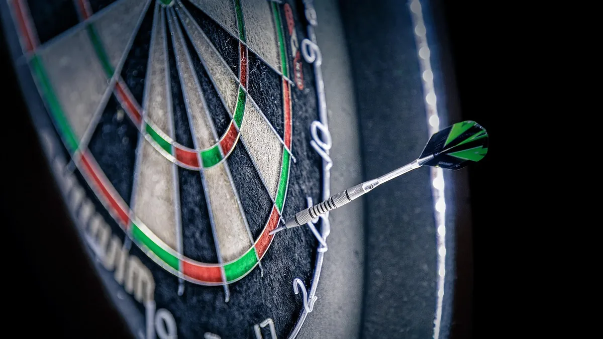 A green-fletched dart precisely strikes a colorful dartboard against a dark background, symbolizing target accuracy.
