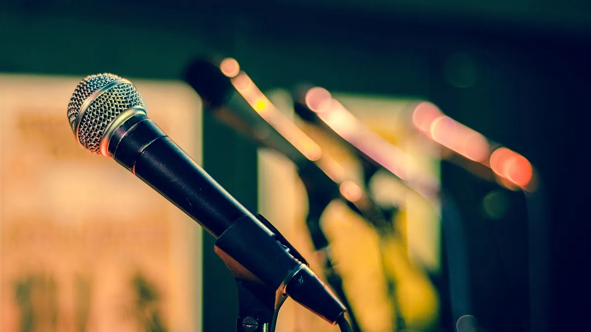 A sharp close-up of a microphone on a stand with soft bokeh lights in the blurry background.