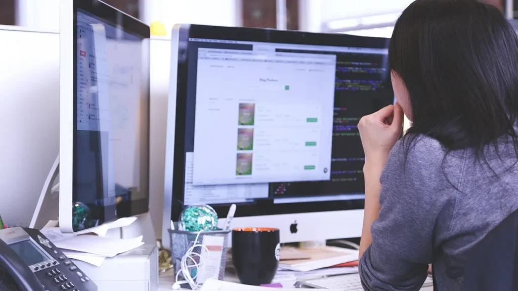 A developer concentrates on code and a web interface on a dual-monitor desk setup.