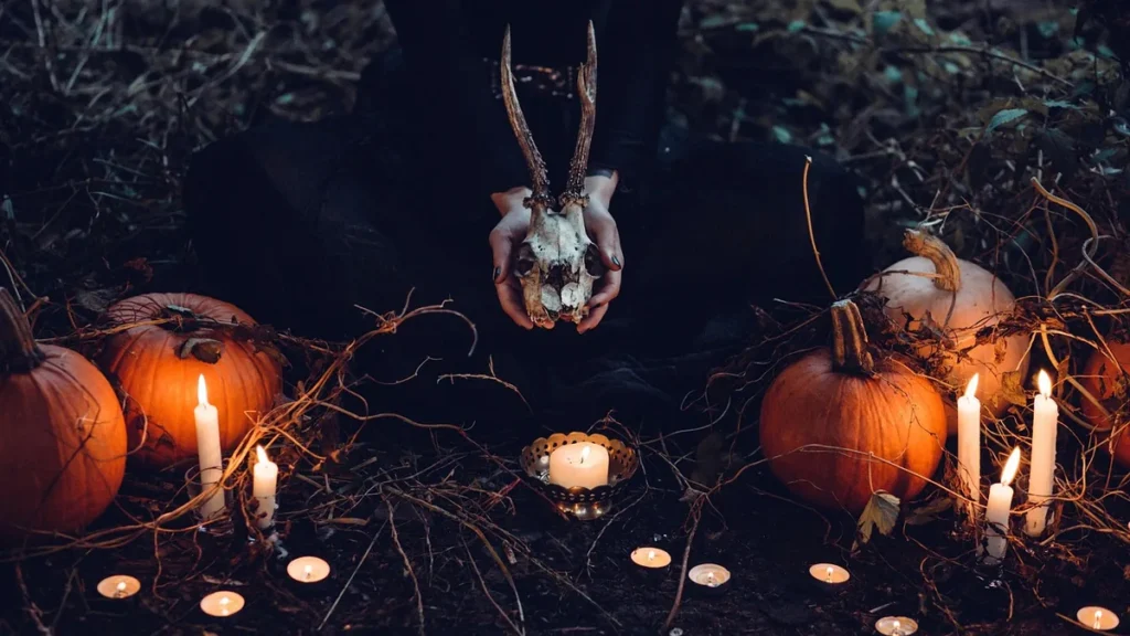 Spooky Halloween ritual scene with pumpkins, burning candles, and hands holding an antlered skull.