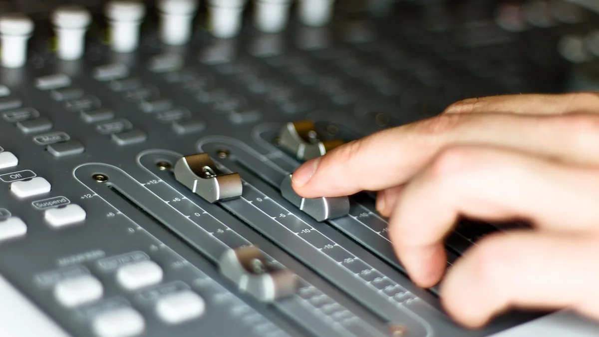 Close-up of a hand adjusting faders on a professional audio mixer, symbolizing music production.