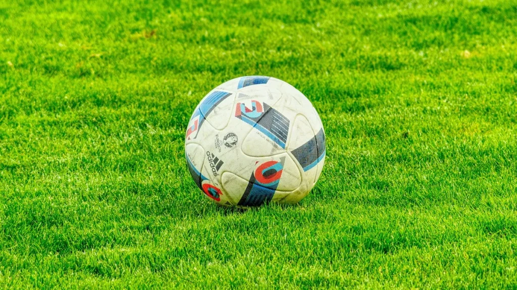 Soccer ball with colorful patterns resting on a lush green grass field under bright daylight.