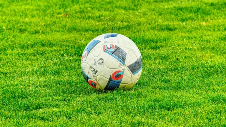 Soccer ball with colorful patterns resting on a lush green grass field under bright daylight.