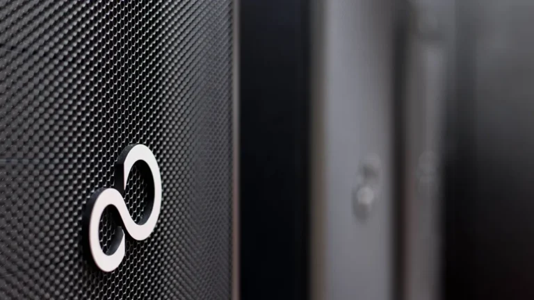 White Fujitsu logo on a black mesh server panel, with blurred server racks in the background.