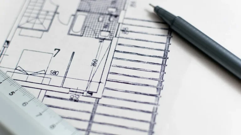 Architectural blueprint close-up with a ruler and black pen, showing technical drawings and measurements.