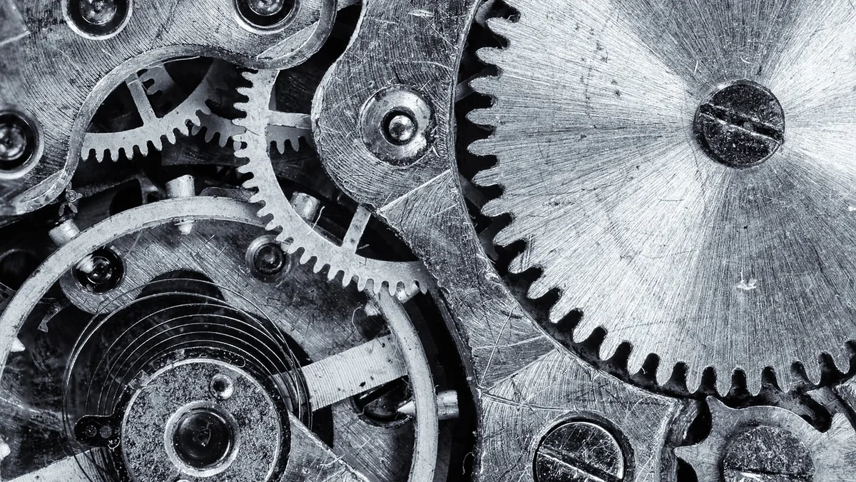 Black and white macro shot of interlocking metallic gears and cogs in a clockwork mechanism.