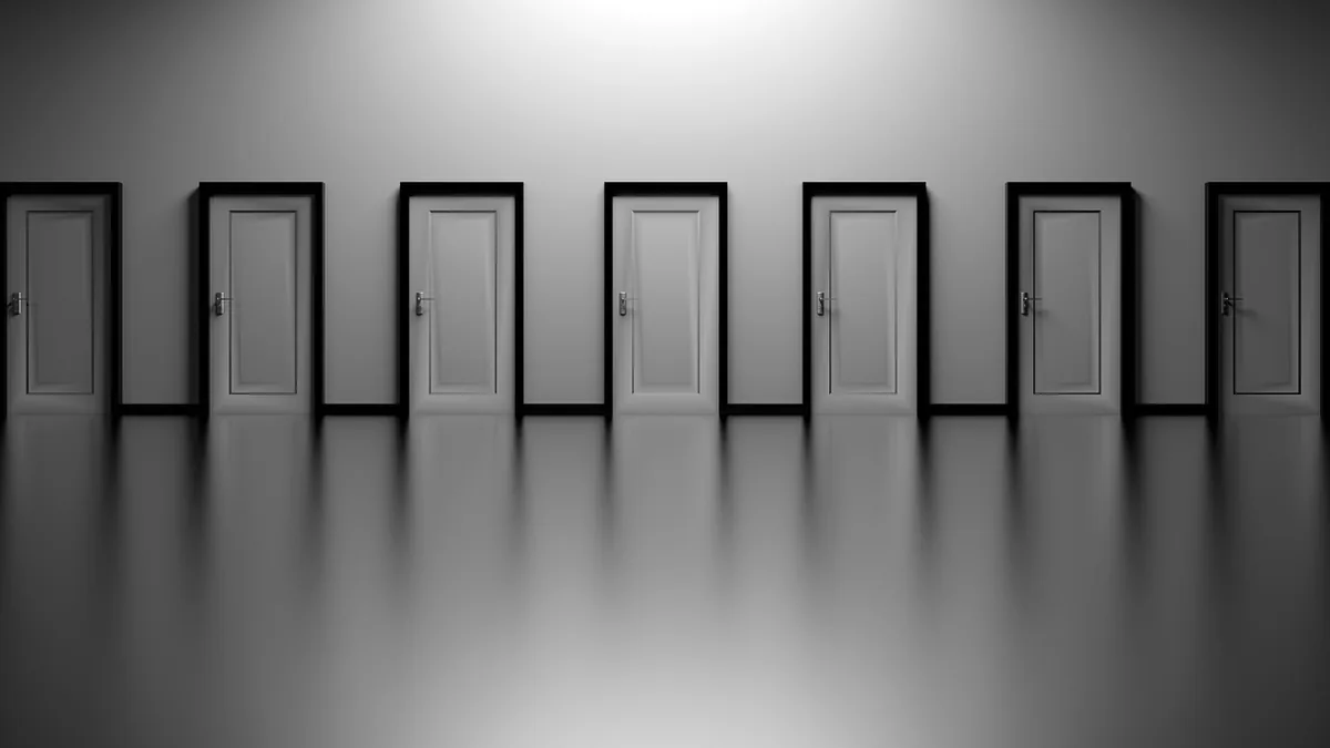 A row of seven grey doors with black frames reflecting on a polished, glossy floor.