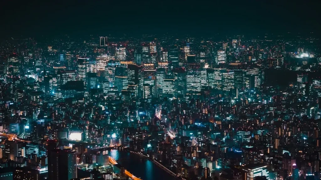 Night view of a sprawling city glowing with teal and orange lights, with a river and bridge below.