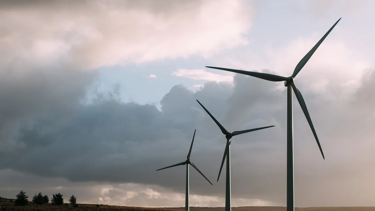 Three wind turbines stand against a dramatic cloudy sky on a grassy hill.