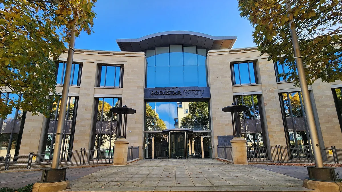 The exterior entrance of the Rockstar North building, showing the company logo on the facade under a blue sky.