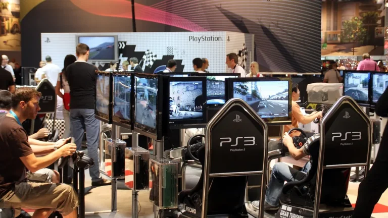 Gamers play racing games on PS3 simulator seats at a crowded PlayStation exhibition booth.