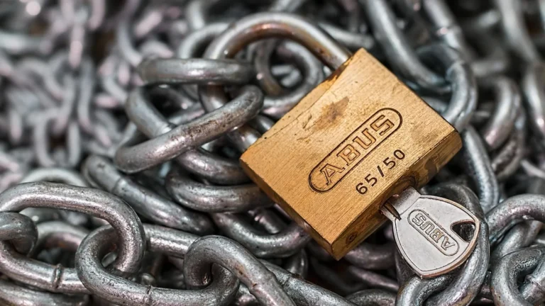 A brass ABUS padlock with key inserted, resting on a pile of heavy metal chains.