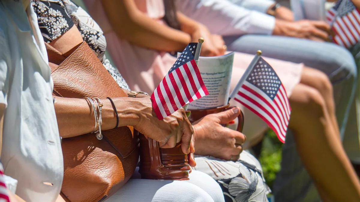 People sitting in a row, holding small American flags and a brown mug during a patriotic event.