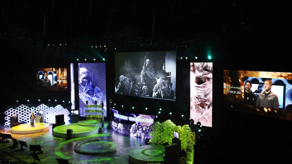 A green-lit stage presentation for Modern Warfare on Xbox 360 with large screens showing soldiers.