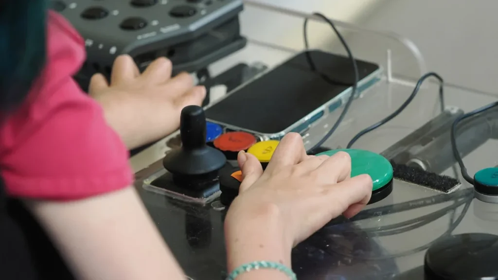 Hands operating a colorful adaptive gaming controller with a smartphone integrated, showcasing accessible gaming technology.