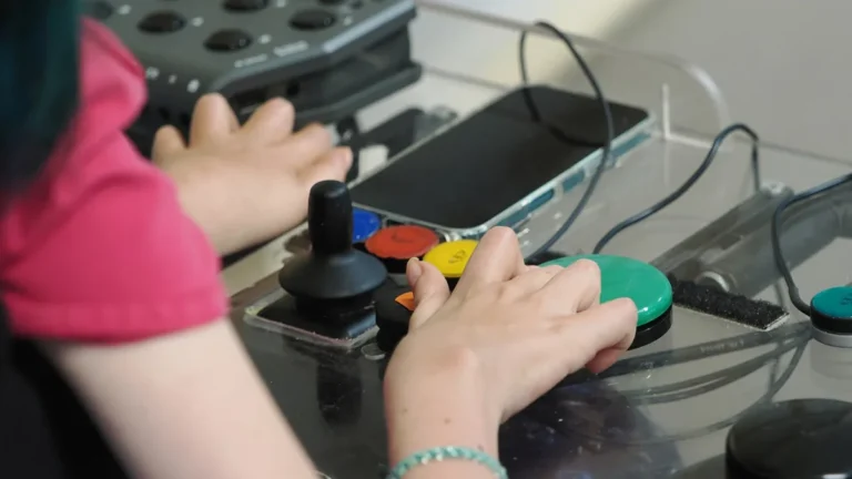 Hands operating a colorful adaptive gaming controller with a smartphone integrated, showcasing accessible gaming technology.